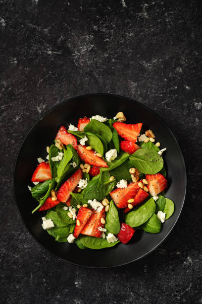 istock Strawberry and spinach spring salad on black background 1209321823
