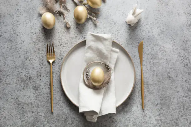 Elegant Easter table setting with golden eggs and bunny on grey stone table. Top view.