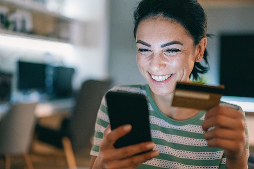 Young smiling woman using smart phone and credit card at home