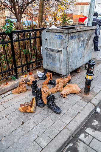 Bursa, Turkey - December 27, 2019: Many pairs of old boots next to a garbage bin in Bursa, Turkey.
