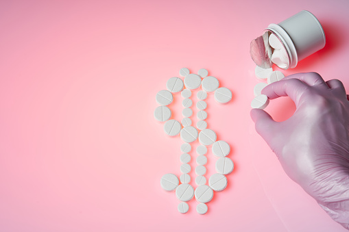 Dollar mark made by white pills spilling out of white bottle on pink background and the doctor holds a white pill. Medicine concept for bussiness.