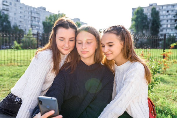 3 teenage girls recording video photograph on phone. In summer city. Emotions happiness, joy, fun, smile. Selfie photo. Portrait a smartphone. Social networks video clip Internet. Online application. stock photo