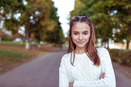 Portrait of a teenage girl of 12 years old, in summer in park, casual clothes, white knitted sweater, free space for copy text. Weekend break. Emotions of happiness are smiles and positive
