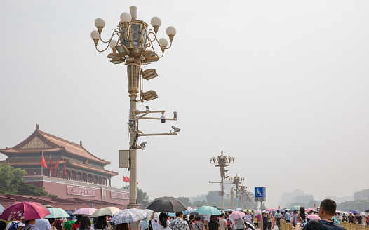 Beijing, China - July 13, 2019: Mass tourists around the Tiananmen Gate Tower in a hot, hazy summer day in Beijing, China. Tourist attraction. Lamp post with surveillance cameras.