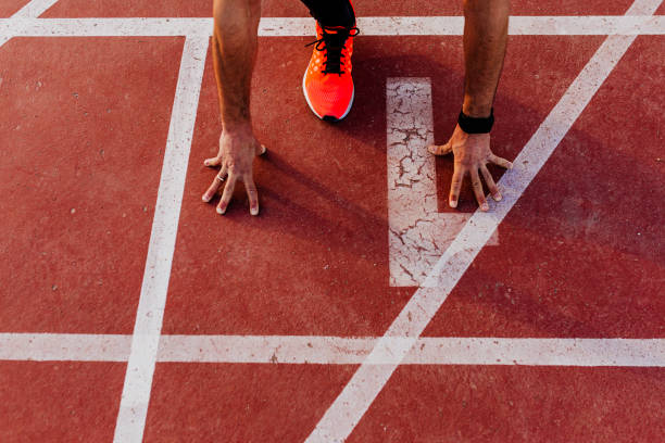 vista de cerca de joven atleta musculoso está en el inicio de la línea de pistas de carreras en el estadio. concepto deportivo - running speed track event jogging fotografías e imágenes de stock