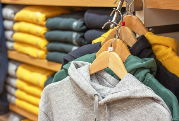 Multicolored hoodie hang on hangers against background of shelves with clothes in the store. stock photo