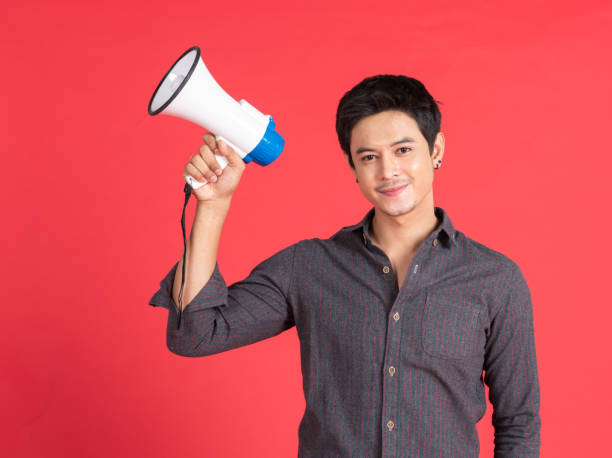 Young asian handsome man screaming with megaphone on red background in studio shot.