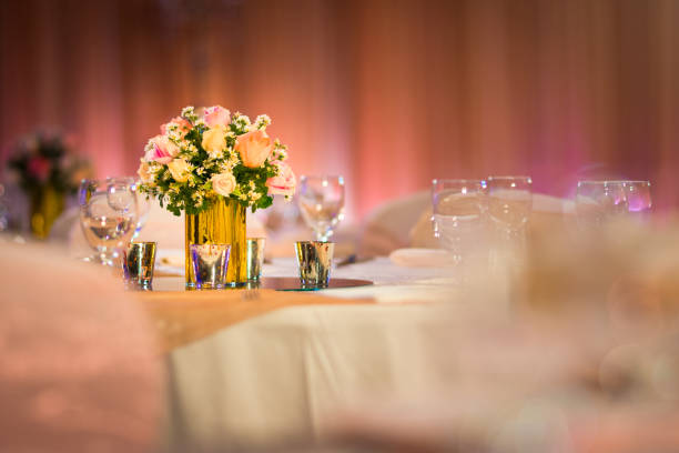 rose florist in glass vase decoration on dinner table with silverware and candle Indian wedding setup indoor with decorative lights and beautiful bokeh.