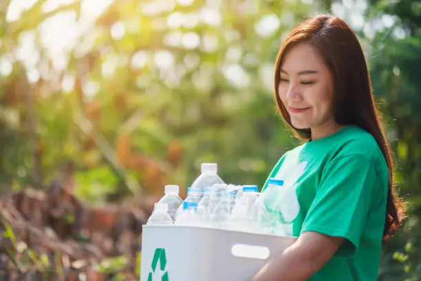 Photo of woman collecting garbage and holding a recycle bin with plastic bottles