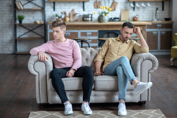 istock Two men sitting on the sofa not loooking at each other looking upset 1209387648