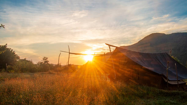 Golden sun rays peaking over the mountains next to a camping tent setup in the paddy field at Pitiwala rural village, Riverston, Matale, Sri Lanka stock photo