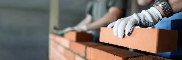 Two workers making red brick wall at construction site close-up