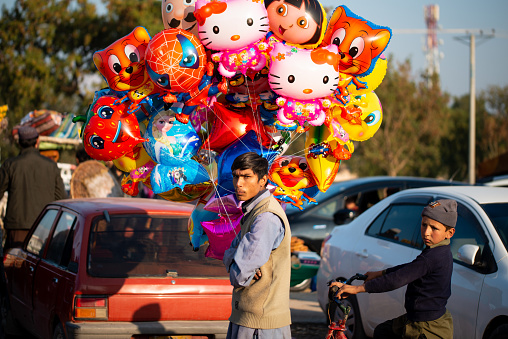 A man on a street selling colorful helium balloons.