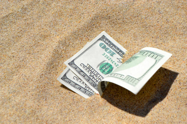 istock Money dollars half covered with sand lie on beach close-up. 1209405995