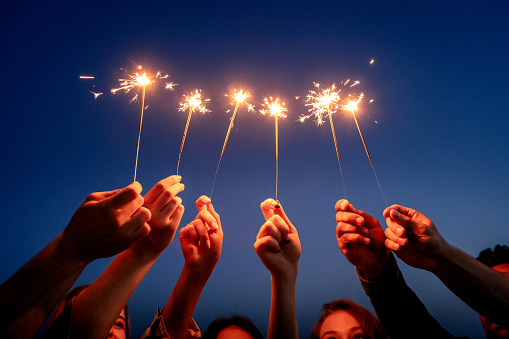 Close up of young people hands holding sparklers against sky.