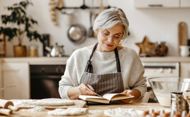 счастливая старуха бабушка повара на кухне месит тесто, печет печенье - grandmother domestic life cooking domestic kitchen стоковые фото и изображения