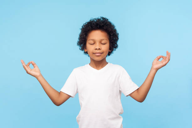 Portrait of peaceful cute little boy holding fingers in mudra gesture and meditating with closed eyes, feeling calm positive Portrait of peaceful cute little boy holding fingers in mudra gesture and meditating with closed eyes, feeling calm positive and relaxed, yoga practice. indoor studio shot isolated on blue background mindfulness kids stock pictures, royalty-free photos & images