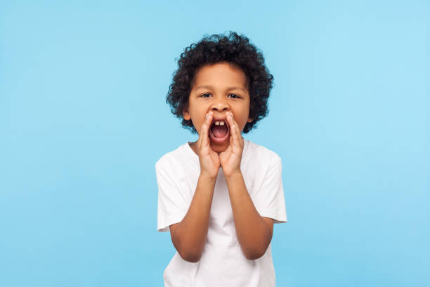 aufmerksamkeit! porträt eines kleinen jungen mit lockigen haaren in weißem t-shirt, das die hände in der nähe des weit geöffneten mundes hält und laut schreit - open concept audio stock-fotos und bilder