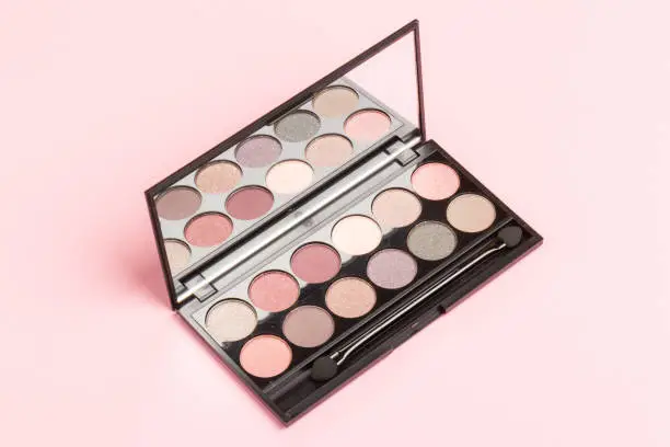The concept of makeup and office dresscode. nude palette of shadows with beige, rose and brown shades on rose background top view