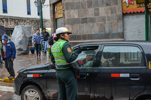 Cusco, Peru - October 25, 2018: police officer checks out passing car on street in Cusco by rainy day.