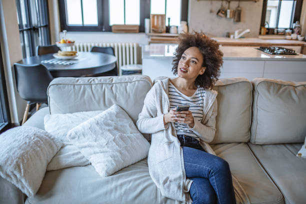 istock Young woman using a smart phone while relaxing on the sofa at home 1209433956
