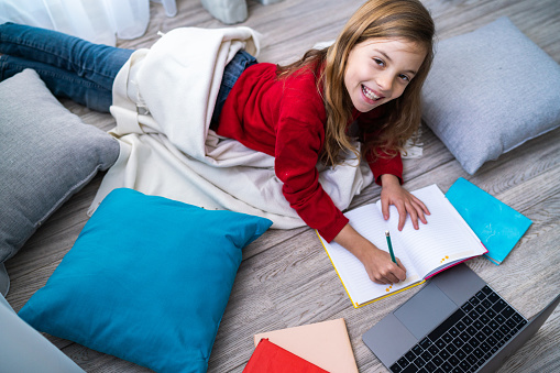 Smiling cute girl is lying on the floor and writing in her notebook