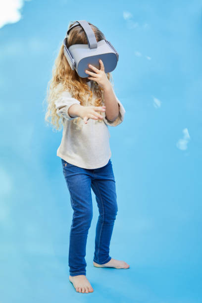 istock Little girl standing on a blue background wearing a VR headset 1209449502