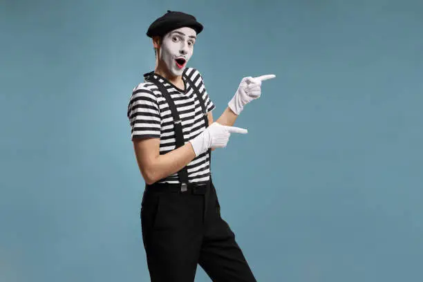 Mime pointing with both hands isolated on a blue background