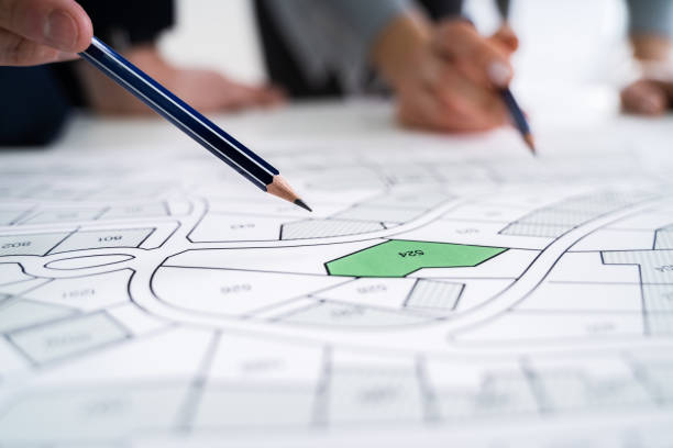 istock Human Hand Holding Pencil Over Cadastre Map 1209449889