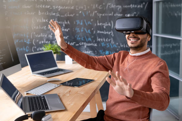 istock Happy young programmer wearing vr goggle sitting by desk with laptops 1209452757