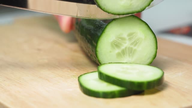 man with his hands cuts a cucumber with a knife on a wooden cutting Board. ingredient for salad. close-up, selective focus