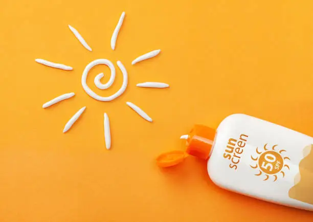 Photo of Sunscreen on orange background. Plastic bottle of sun protection and white sun-shaped cream.