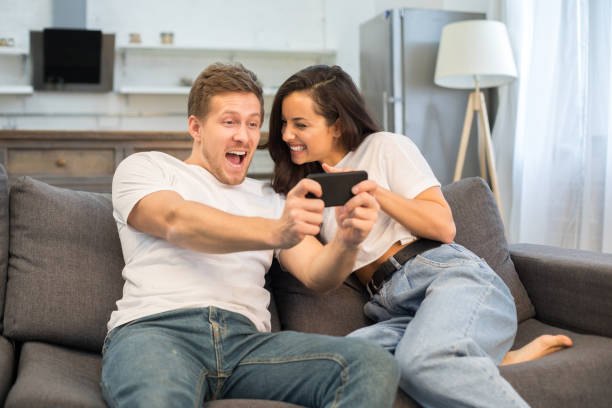 istock Happy young couple using smartphone in their living room 1209458552