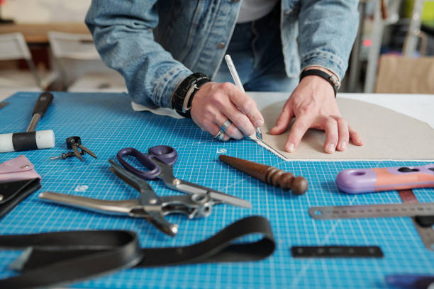 istock Hands of young craftsman bending over table while outlining paper pattern 1209459848