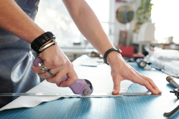 istock Hands of creative professional leatherworker cutting piece of white leather 1209459853