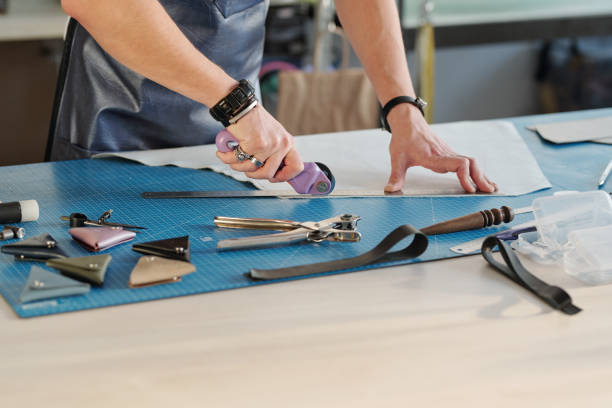 istock Hands of young leather worker using cutter while holding ruler on piece of suede 1209459862