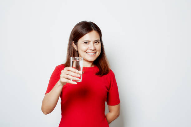 istock Young smiling woman drinks water from a glass isolated studio portrait on white 1209460895
