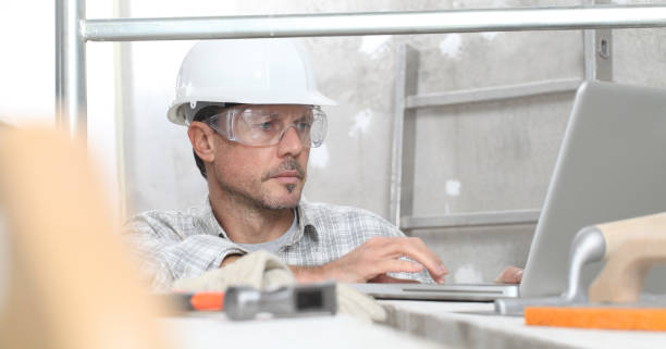 mann arbeit, professionelle bauarbeiter mit computer, putzwerkzeuge auf gerüsten, sicherheit hart hut, handschuhe und schutzbrille. auf der innenbaustelle hintergrund - building contractor computer internet construction worker stock-fotos und bilder