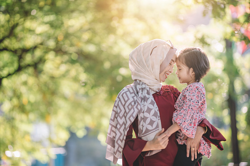 an asian modern muslim malay woman with hijab and sunglasses carrying her daughter outdoor on the street of kuaala lumpur bonding time