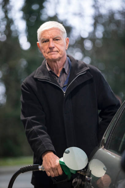 senior adult man fueling car gas tank and looking at camera - old men car oil imagens e fotografias de stock