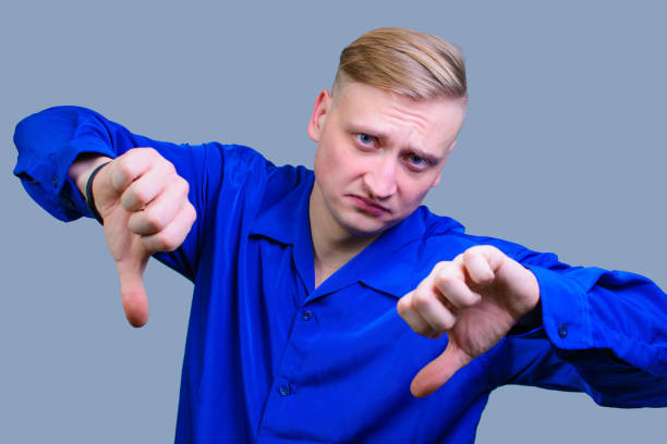 istock Young handsome guy with blond hair shows a thumbs down with both hands. 1209469762
