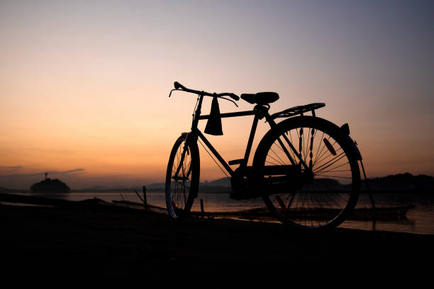 una bicicletta sulle rive di un fiume al tramonto - wheel cycling nobody outdoors foto e immagini stock
