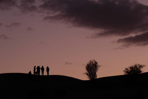 istock Dramatic silhouette view of people standing on a dune at sundown 1209471957