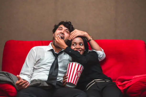 Happy diversity love couple man and woman with popcorn watch cinema in movie theater