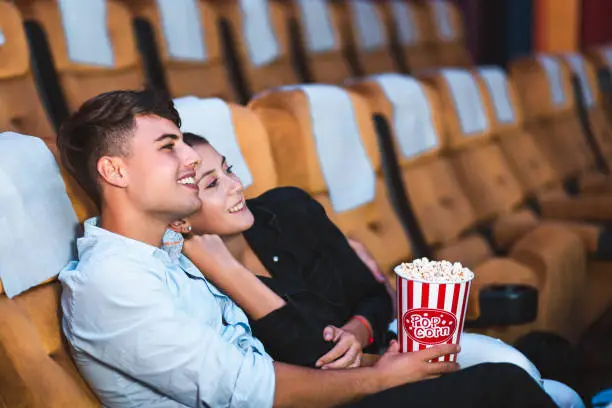 Happy young love couple with popcorn watch cinema in movie theater