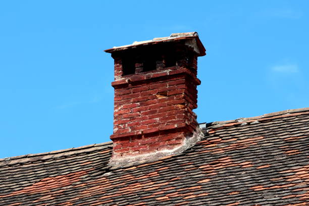 istock Single elongated narrow old dark red bricks dilapidated cracked chimney with multiple openings covered with small roof tiles 1209481688