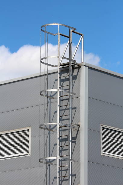 istock Vertical access ladders with round safety tunnel for use as emergency fire escape on side of new industrial building 1209481723