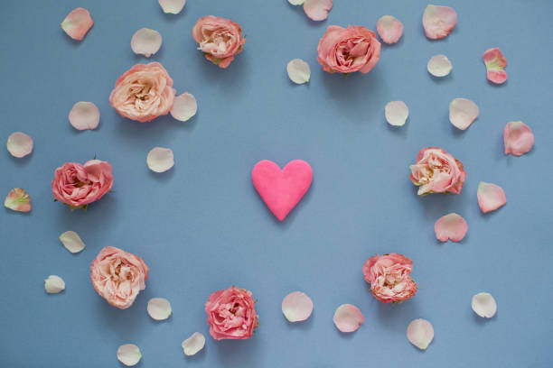 istock Bright pink heart inside frame of roses and petals on a blue background 1209485518