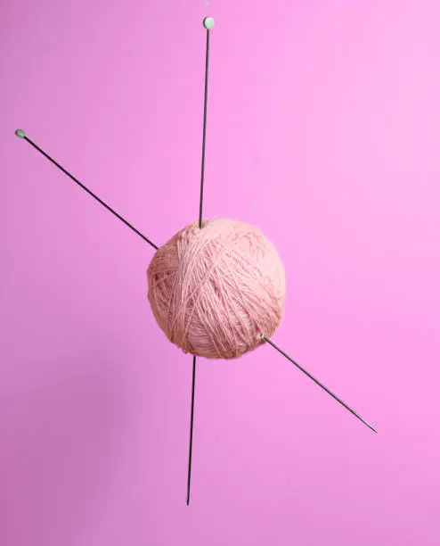 Home hobbies concept. Wool balls of thread with knitting needles on pink background.