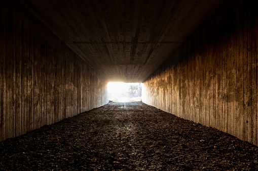 Rough concrete pedestrian gravel footpath underpass. Perspective architecture with light at the end of the tunnel. Sunshine outside lighting up tunnel walls, Jarfalla Sweden.